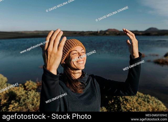 Happy woman with arms raised standing by lake