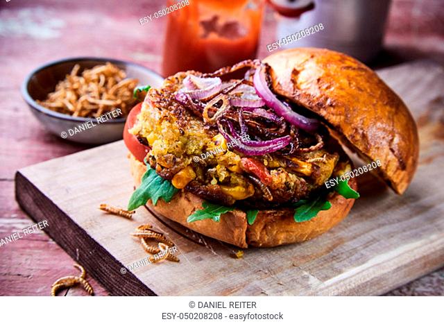 Speciality insect burger with fried mealworms and salad trimmings with rocket on a crusty fresh bun served on a wooden board suitable for a menu