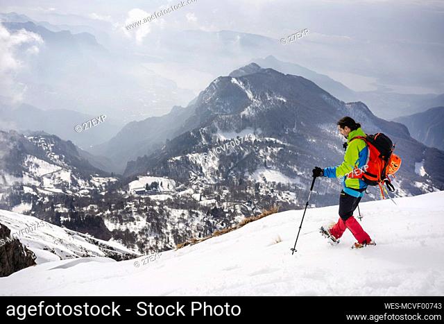Male trekker with backpack and hiking pole walking on snowcapped mountain wearing crampon