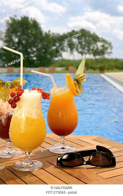 Three cocktails and sunglasses on a table next to a swimming pool