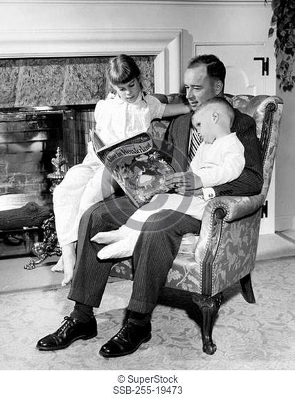 Father reading Alice in Wonderland to daughter and son