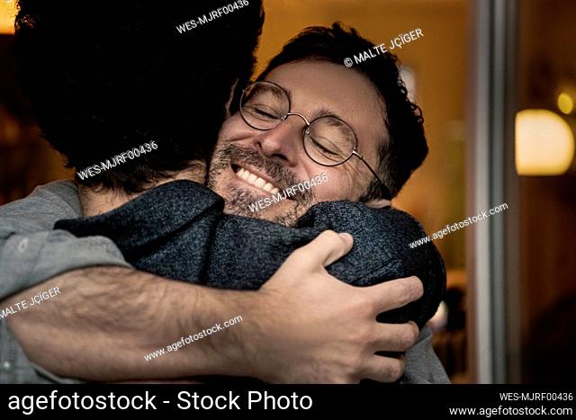 Smiling mature man embracing male friend at home