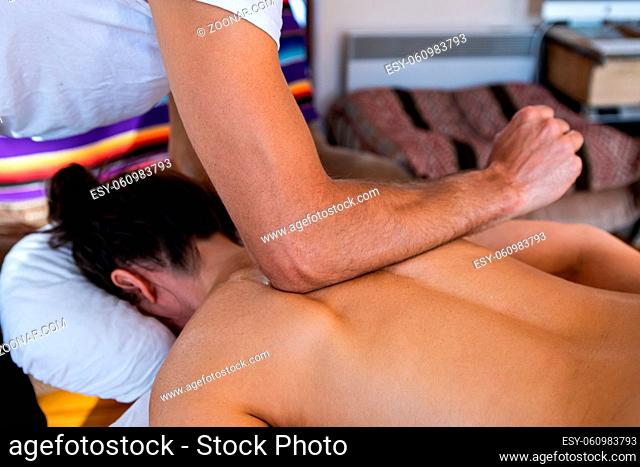 Spa massage for woman. Young female enjoying a relaxing back massage in a cosy home environment. Medium shot of massaging process