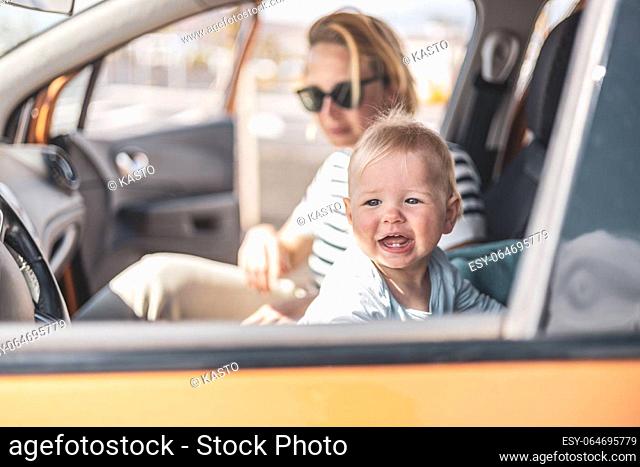 Mother and her infant baby boy child on family summer travel road trip, sitting at dad's front seat, waiting in the car for father to buy farry tickets