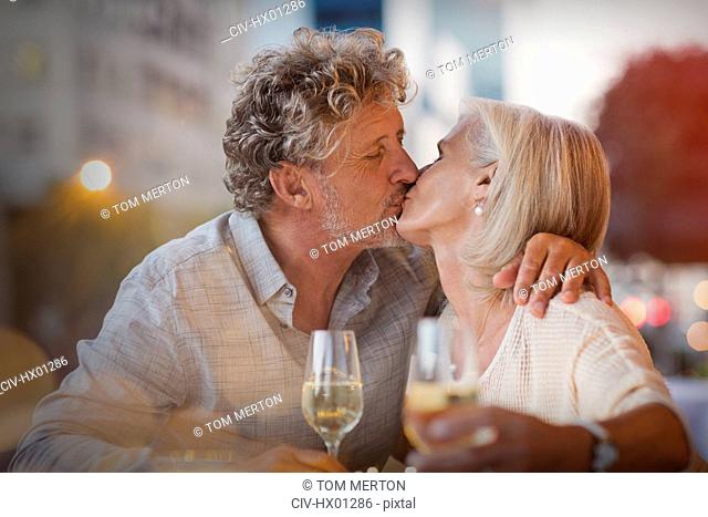 Affectionate senior couple kissing drinking white wine at sidewalk cafe