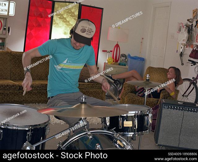 portrait of young garage band drummer practicing with friend in background