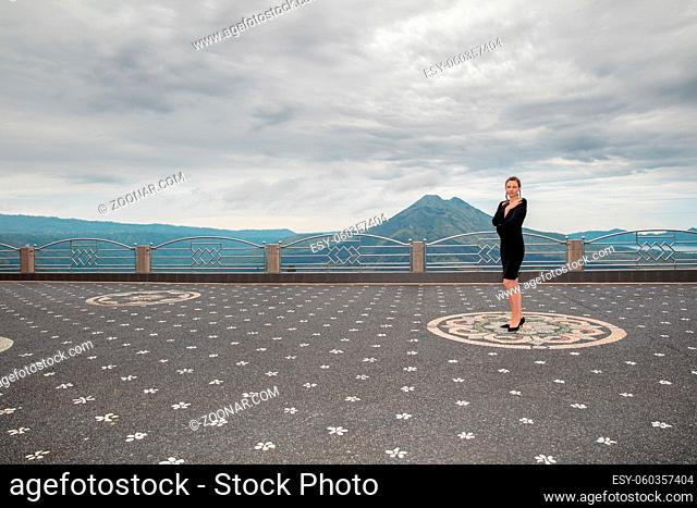 Lovely woman wearing in black dress against the backdrop of the volcano Batur, Bali Island, Indonesia