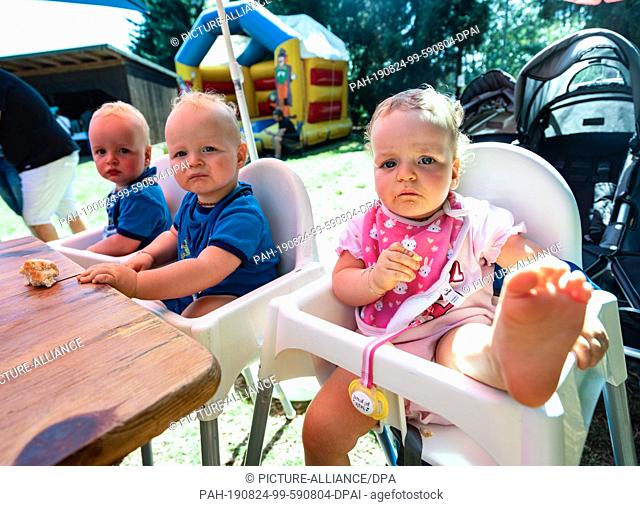 24 August 2019, Hessen, Lich: The 14-month-old triplets Thies (l-r), Bennett and Leonie sit on their high chairs at the triplet meeting of the Hessian Prime...
