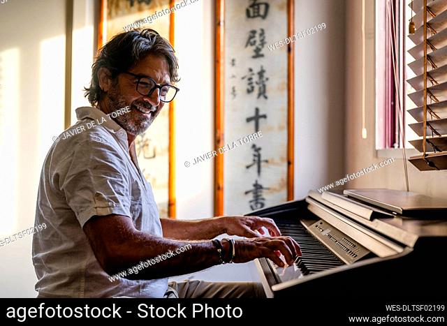 Smiling mature man playing piano at home