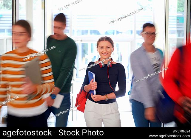 portrait of a happy young student getting ready for class while waiting in the college hallway with headphones and notes