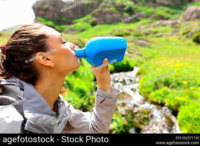Trekker drinking water from canteen beside a creek in the mountain
