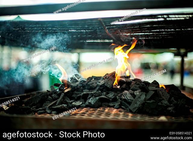 A close up and side profile view with soft focus on the burnt kindling and flames of an outdoor BBQ grill. Cooking outdoors. Copy space to sides