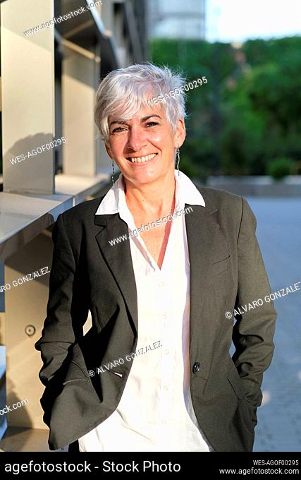 Smiling mature businesswoman near railing on sunny day