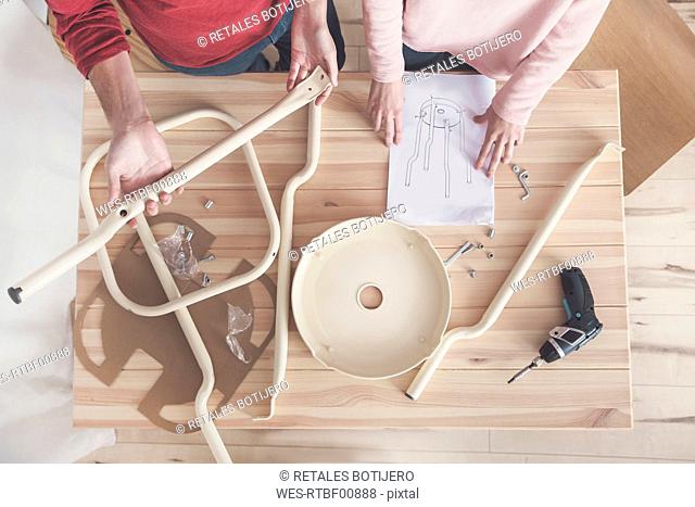 Young couple assembling flat-pack stool at home, partial view