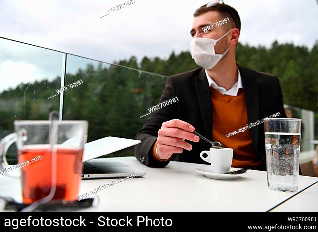 man sitting separated in restaurant drinking coffee wearing medical protective face mask to protect infection from coronavirus covid-19