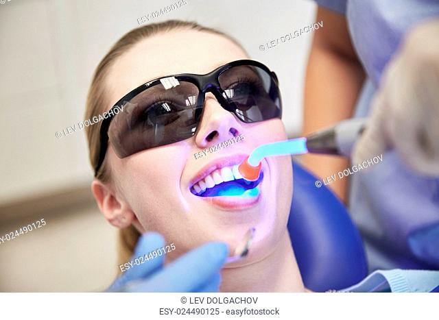 people, medicine, stomatology and health care concept - close up of woman patient in protective eyeglasses or goggles with dental curing light treating teeth at...
