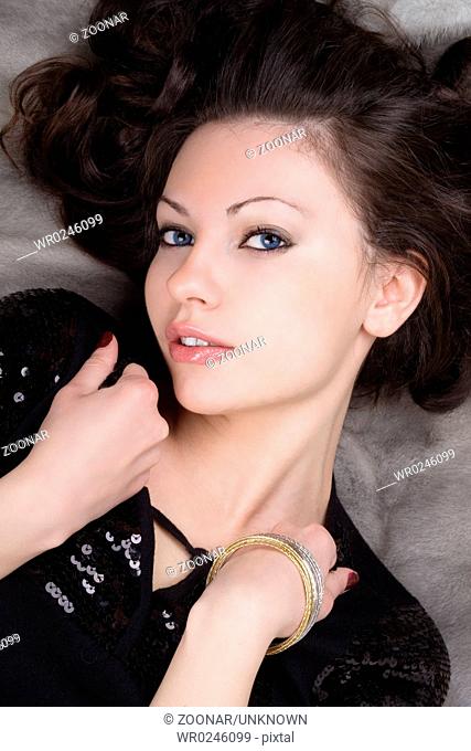 Portrait of the beautiful girl lying on grey fur coat