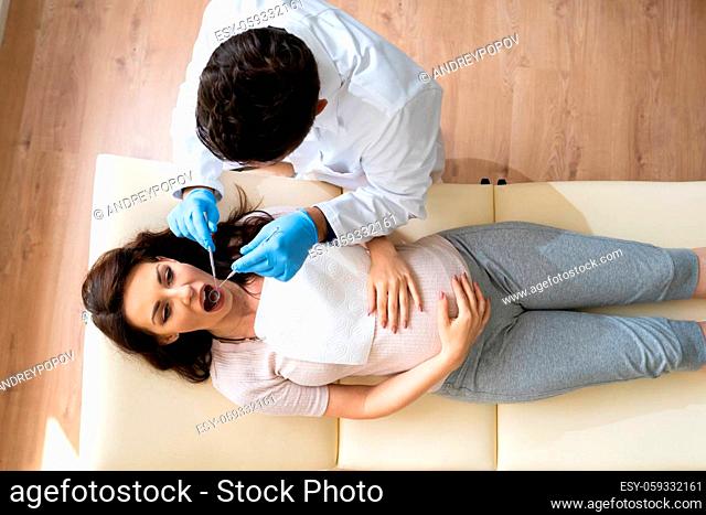 Dentist Treating Teeth Of Young Pregnant Woman Patient Lying In Clinic