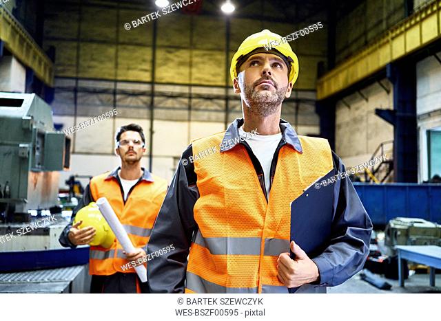 Two men wearing protective workwear looking around in factory