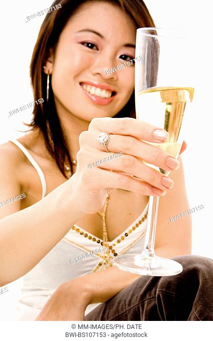 A young asian woman lifts her glass of champagne for a toast (focus is on the glass)
