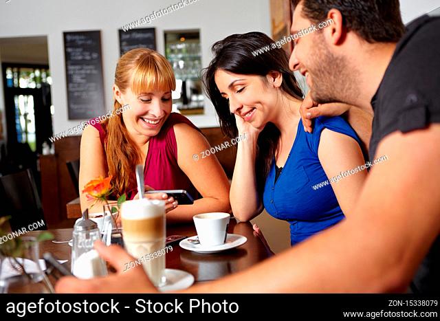 Drei Freunde schauen auf Handy Fotos an im Café