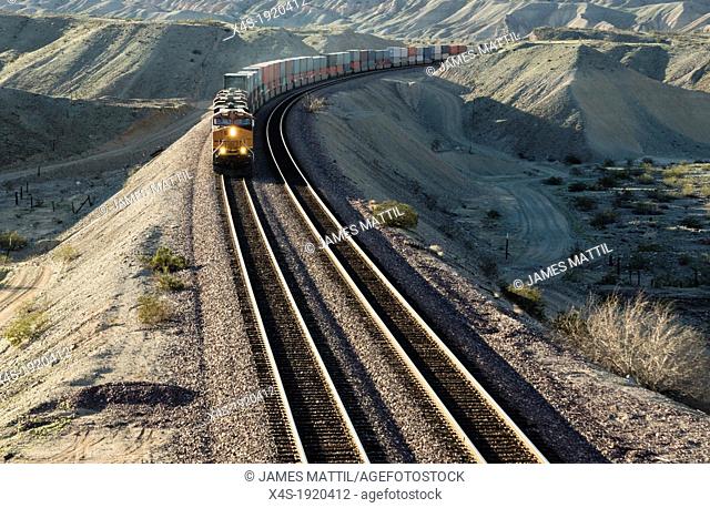 A frieght train rounds a bend in the aride California desert in late afternoon