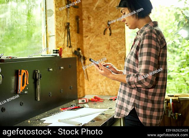 Female business owner using digital tablet in workshop, industrial woman engineer working with blueprints and tablet in the workshop