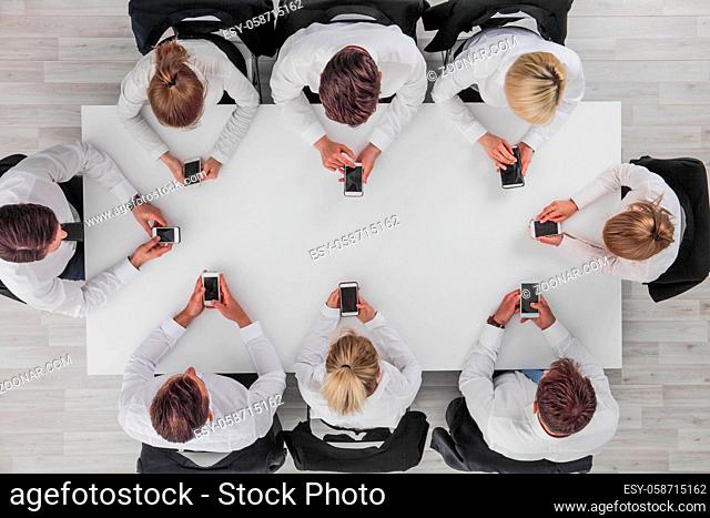 Top view of business people sitting around the table and using smartphones with blank screen