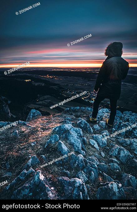 Hiker with backpack relaxing on top of a mountain and enjoying sunrise in austrian alps