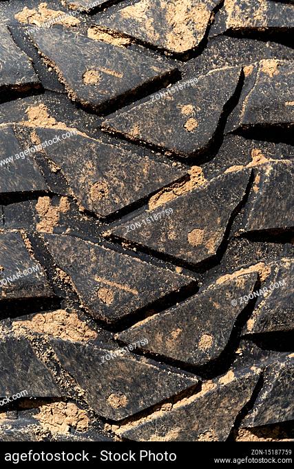 Close-up view of old used rubber mud terrain tire with worn wear-resistant tread. Black muddy sport utility vehicle tire with adhering dirt after overcoming an...