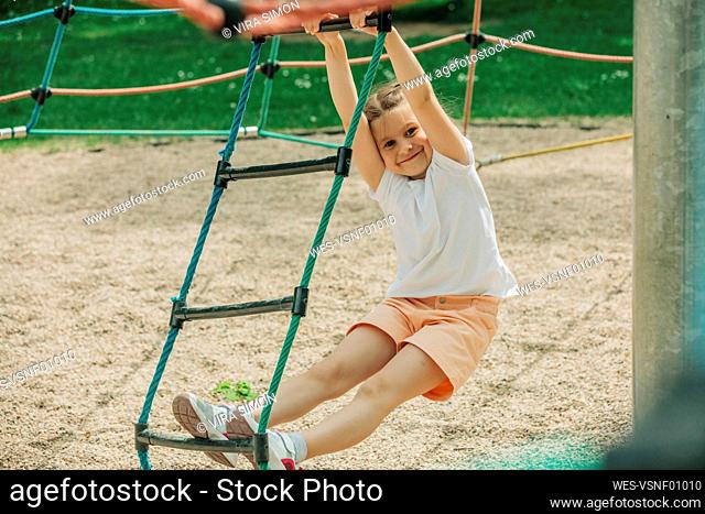 Smiling girl climbing rope ladder at playground