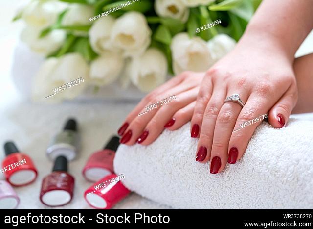 Close-up of the hands of a young woman with red polished nails and rhinestones applied in a trendy beauty salon
