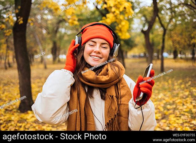 Smiling young woman with eyes closed enjoying music through headphones at park