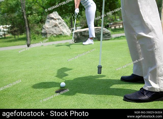 Low section view of man and woman golfing and putting on the golf course