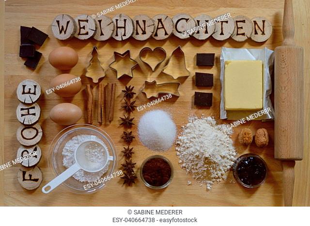 Baking ingredients for christmas cookies on a bread board with wooden pieces and the german words FROHE WEIHNACHTEN burned into them