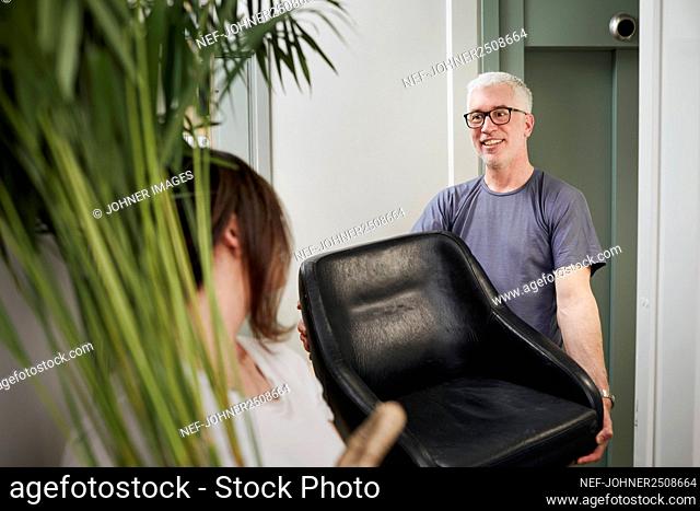Smiling man carrying armchair