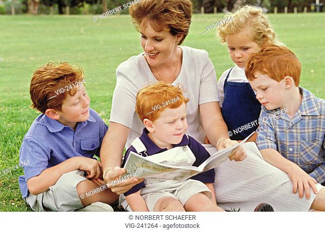 portrait, park-scene, redheaded woman sits with her 4 also redheaded children, 3 boys and 1 girl, 3-7 years, on a meadow reading a picture book to them  -...