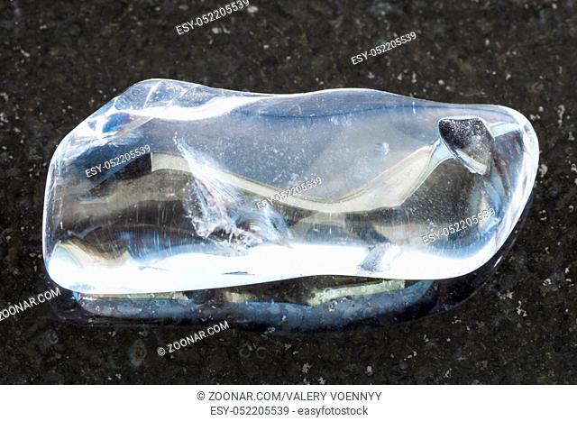 macro shooting of natural mineral rock specimen - tumbled clear Quartz (rock-crystal) gemstone on dark granite background