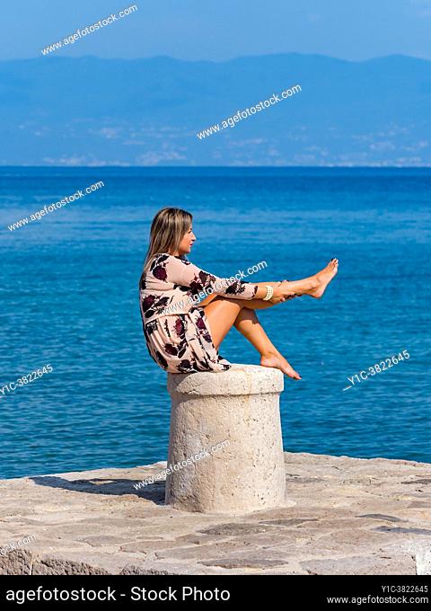 Young woman sitting on bollard is looking at raised leg