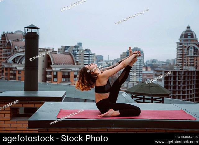 Young woman practicing yoga on the mat on the roof and doing yoga exercises