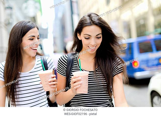 USA, New York City, two happy twin sisters on the go in Manhattan with takeaway drink
