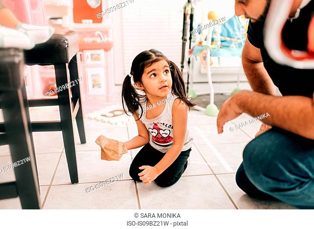 Girl wiping kitchen floor, father watching