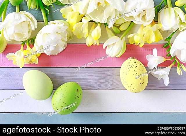 Tulips and freesias on white wooden table. Easter eggs among flowers, copy space