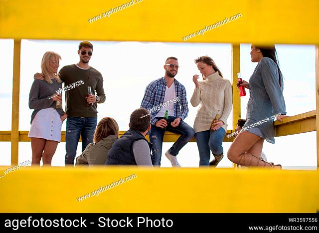 Happy Group Of Friends Hanging Out At Beach House having fun and drinking beer on autumn day