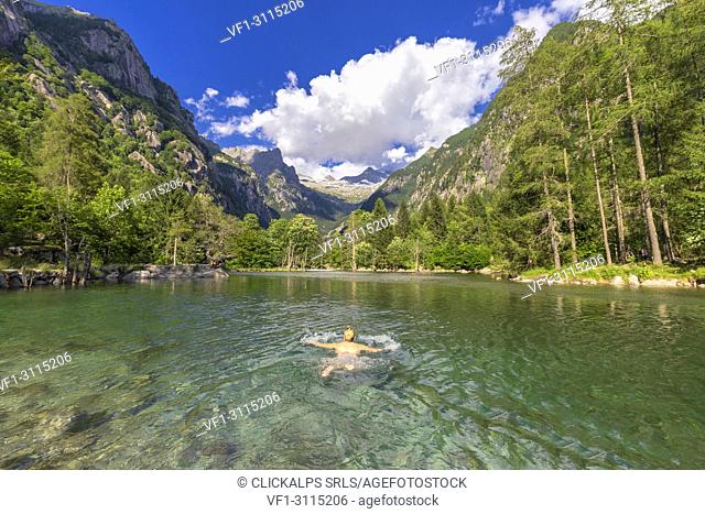 A girl swims in a clear alpine lake. Val di Mello(Mello Valley), Valmasino, Valtellina, Lombardy, Italy, Europe