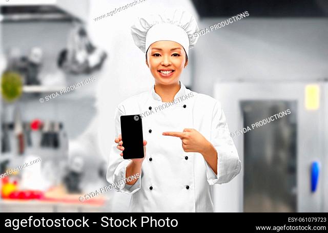 smiling female chef with smartphone in kitchen