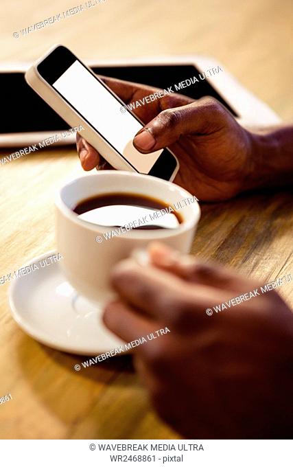 Hand using smartphone while taking a cup of coffee in the restaurant