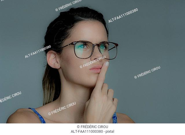 Young woman looking away in thought with finger held to lips
