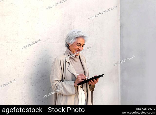Happy woman using digital tablet in front of wall
