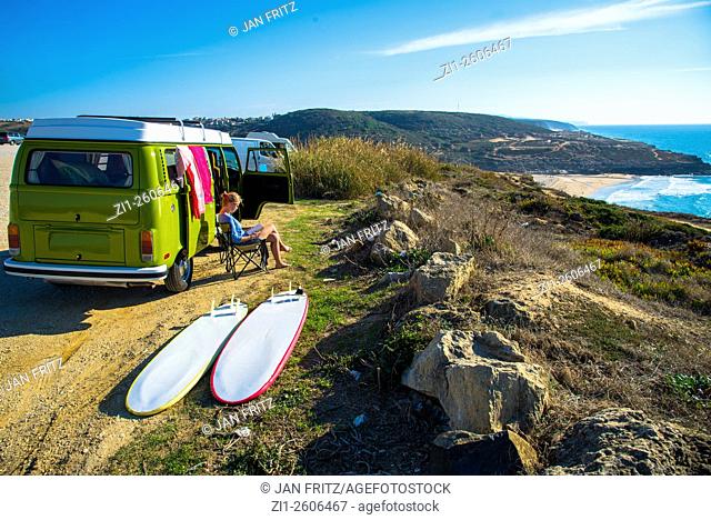 young woman sit and read next to camper with surfboards with view at the coast of Portugal